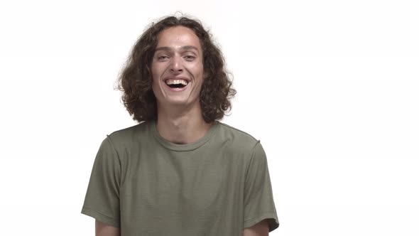 Handsome Brunette Guy with Wavy Messy Hairstyle Wearing Tshirt Hearing Something Funny and Laughing