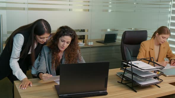 Three happy diverse women two having teamwork other looking into documents.