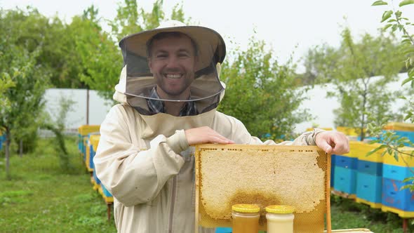 Portrait of Beekeeper with a Honeycomb Frame and Jars with Honey