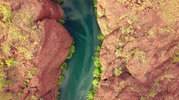 Drone flying high above a red rock gorge/canyon looking straigh down. Drone turns slowly to follow t