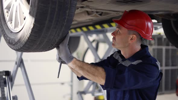 Auto Mechanic Working Underneath Car Lifting Machine at the Garage