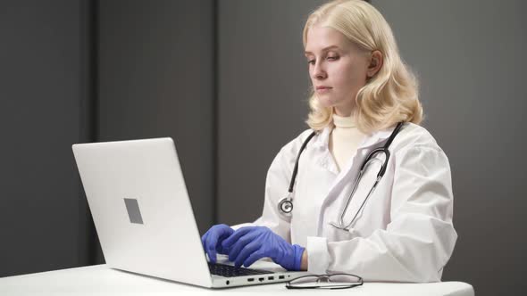 Woman Doctor Working at Computer Entering Data From Patient File