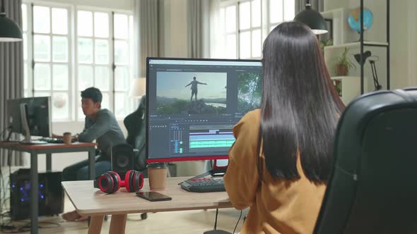 Back View Of Asian Female Video Editor Works With Footage And Sound On Computer In Office