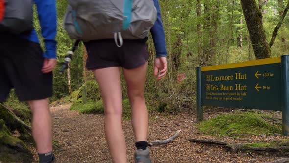 Rear static, hikers walk past Luxmore Hut information sign, Kepler Track New Zealand