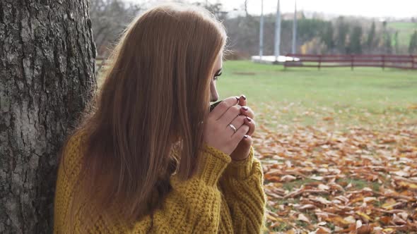 Adult girl is drinking hot beverage at chilly autumn day in slow motion.