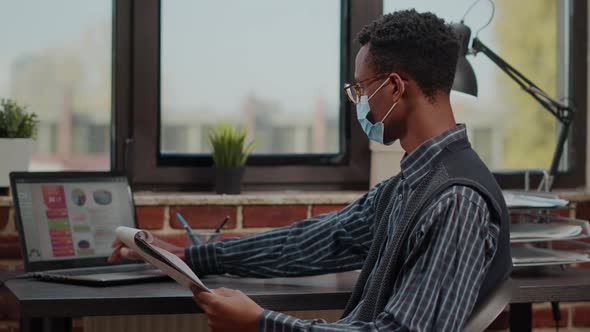 Business Man with Face Mask Analyzing Commercial Data on Laptop