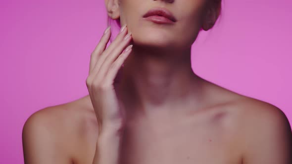 Woman Runs Finger Along Chin After Using Cosmetic Cream While Standing on Pink Background in Studio