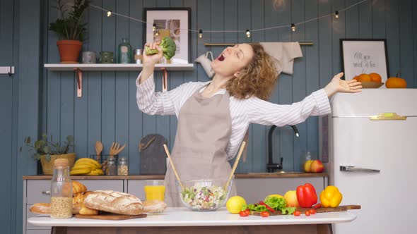 Young Happy Woman Singing And Dancing On Kitchen While Cooking Healthy Food