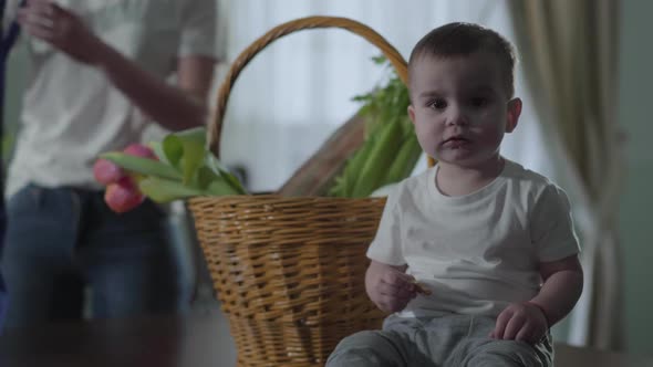 A Little Boy Sits Near the Basket on the Table and Eats