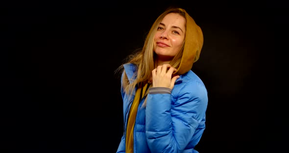 Portrait of a Blonde in a Hoodie and a Blue Jacket on a Black Background