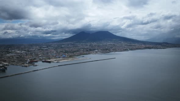 Aerial hyperlapse of clouds flying over Mount Vesuvius while boats drive past on the water.