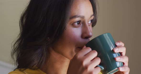 Profile of relaxed biracial woman drinking coffee and looking outside window