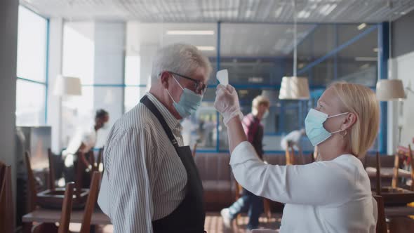 Side View of Mature Restaurant Owner in Face Mask Check Staff Temperature