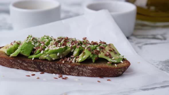 Female Hand Making Healthy Avocado Toast on Wooden Board