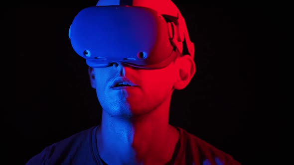 Man in a Virtual Reality Helmet Illuminated in Red and Blue Plays a Game