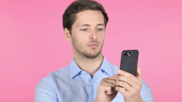 Young Man Using Smartphone on Pink Background