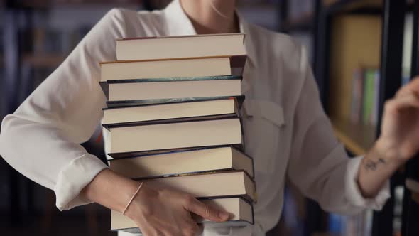 Woman Holding Pile of Books in the Library Putting More on the Stack