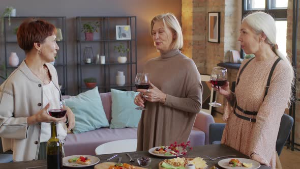 Three Mature Women Toasting with Glasses of Red Wine at Home Party