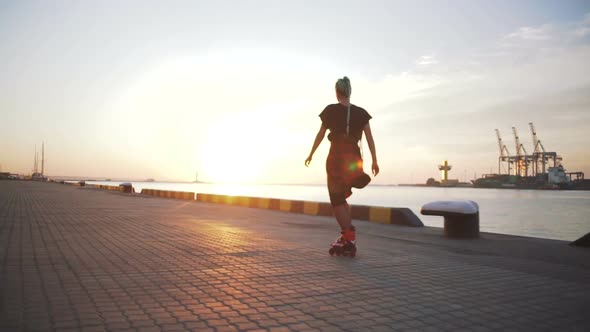 Young Stylish Funky Girl with Green Hair Riding Roller Skates and Dancing Near Sea Port During