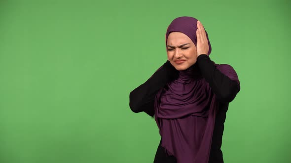 A Young Beautiful Muslim Woman Hears a Loud Noise and Covers Her Ears  Green Screen Background