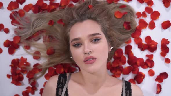 Portrait of a Young Girl with a Piercing on Which Fall Red Rose Petals Close Up