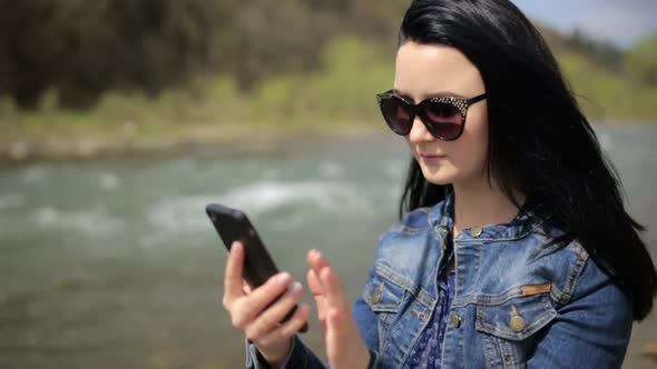 Young Brunette Girl in a Denim Jacket She Uses a Smartphone