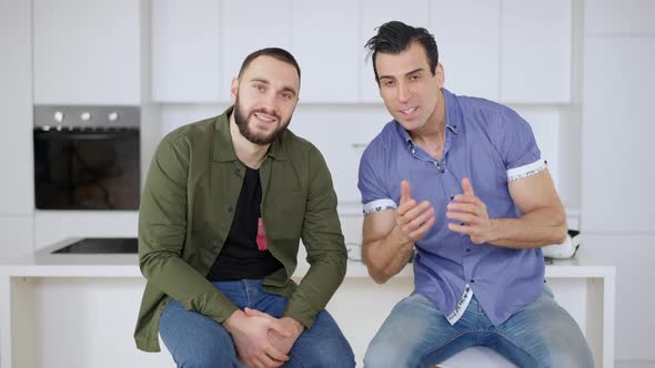 Front View of Two Positive Young Men Watching Comedy Movie on TV Talking and Laughing