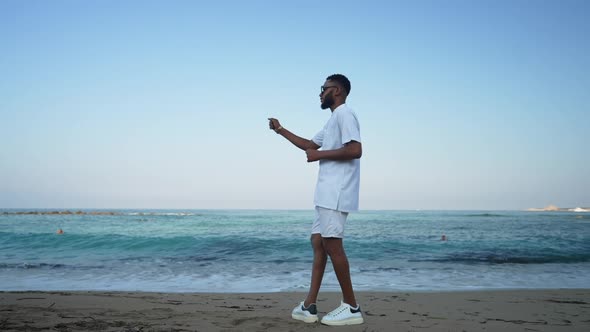 Wide Shot of Joyful African American Happy Man Dancing on Sandy Beach with Turquoise Blue Waves