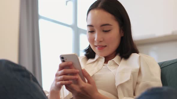 Confident Asian woman texting by phone