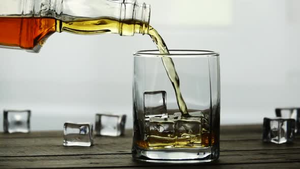 Whiskey Pouring Into a Glass with Ice Cubes on Old Wooden Table in Slow Motion