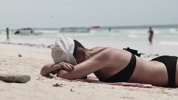 Young Woman Sunbathes on a Paradise Sandy Beach Lying in Black Bikini Near Ocean