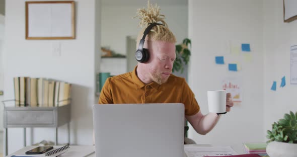Albino african american man with dreadlocks drinking coffee making video call on the laptop