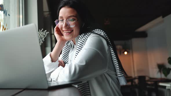 Smiling young brunette woman in eyeglasses talking by video call on laptop