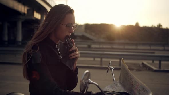 Side View of Attractive Girl in Sunglasses Sitting on Motorcycle Taking Off Gloves Examining Map on