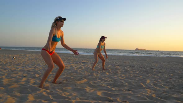 Women teams play beach volleyball at sunset and a player passes the ball.