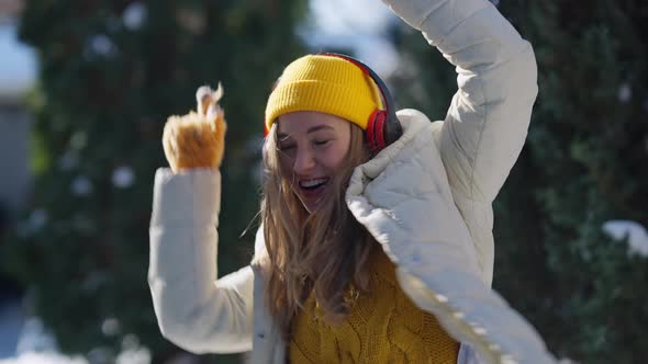 Happy Young Woman Dancing to Music in Headphones Singing on Cold Winter Sunny Day Outdoors