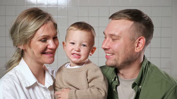 Parents Hold Little Son in Arms Standing Against Wall