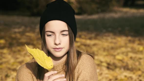 Young Female Teen Poses with Autumn Leaf at Camera in Park