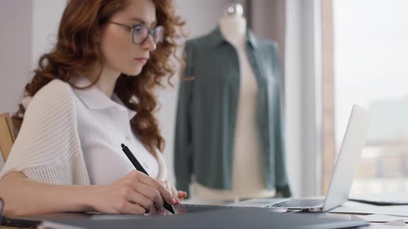 Ginger adult woman using laptop and digital tablet at work. Shot with RED helium camera in 8K