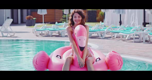 Brunette in Bikini Swimming in Pool on Inflatable Flamingo
