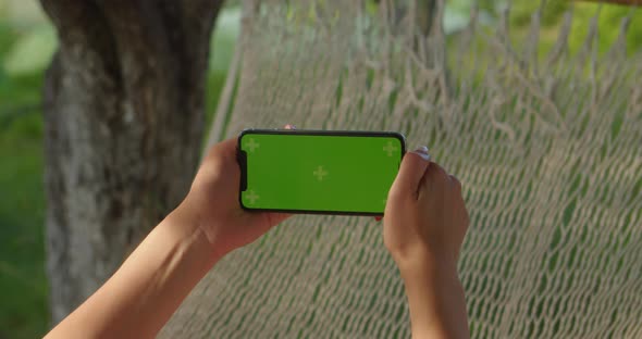 Young Women Rests in Hammock Looking Into Sideways Phone with Green Screen