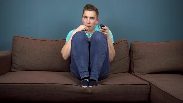 A Young Man Is Watching TV and Eating Popcorn. The Guy Is Watching TV Carefully. An Exciting Moment