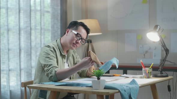 Asian Man Designer With Layout Bond Looking At The Fabric In Hands