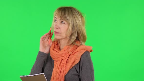 Portrait of Middle Aged Blonde Woman Is Thinking, Then Writing with Pencil in Notebook. Green Screen