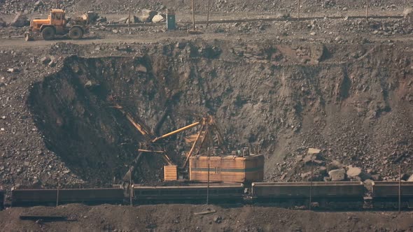 Big yellow excavator loads iron ore onto a mining freight train.