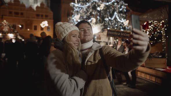 Portrait of Pretty Young Couple Making Selfie Outside with Christmas Decorations Around