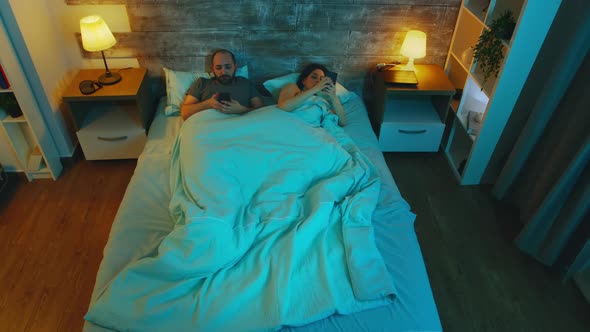 Top View of Couple in the Bedroom Late at Night Using Their Phones