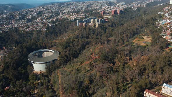 Aerial dolly out of Quinta Vergara Amphitheater in Park covered in woods, Viña del Mar hillside city