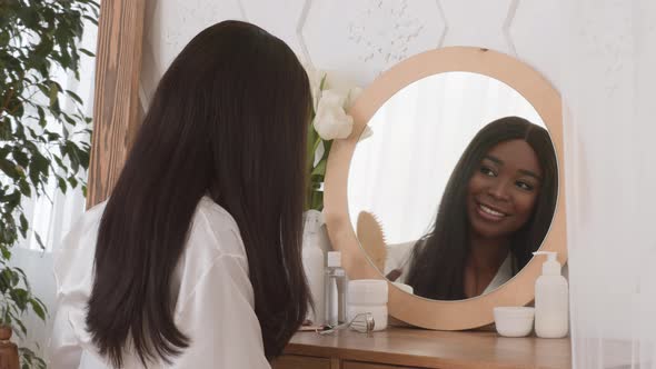 African American Woman Brushing Hair Sitting Near Mirror At Home