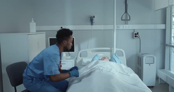 Sad African Doctor Sitting Near Dead Patient Covering Body with Sheet and Closing Curtain